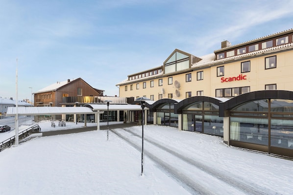 A hotel with a snow-covered ground, a covered outdoor seating area, and a large windowed facade. - Scandic Vadsø (Vadsø)