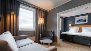 A modern hotel room with a sofa, armchair, and a bed with a headboard. - Scandic Vadsø (Vadsø)