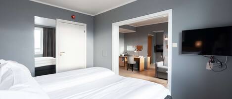 A hotel room with a large bed, a desk, a chair, a TV, and a bathroom visible through an open door.