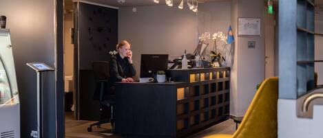 A reception desk with a computer, a plant, and a flag. There is a yellow chair in the foreground.
