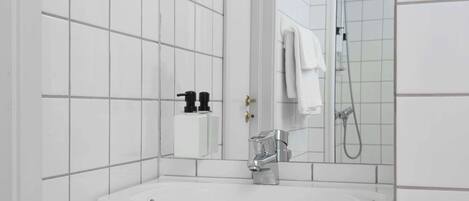 A modern bathroom with white tiled walls, a white sink, a mirror, and a shower area.