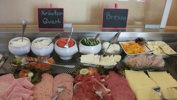 Un bufé con diversas opciones de comida, incluyendo carnes, quesos y ensaladas, identificadas con nombres como 'Kräuter Quark' y 'Bresso'.