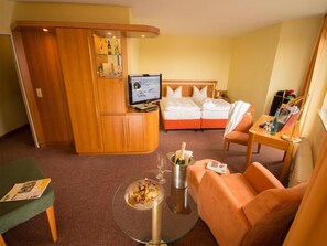 A hotel room with a bed, a TV, a minibar, a seating area, and a small table with a bottle of champagne. - Ringhotel Parkhotel Witten (Witten)