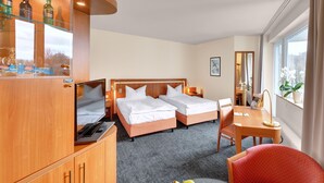 A hotel room with two beds, a desk, a chair, a TV, and a minibar. - Ringhotel Parkhotel Witten (Witten)