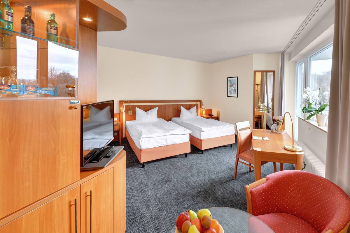 A hotel room with two beds, a desk, a chair, a TV, and a minibar.
