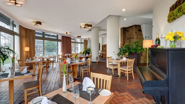 A restaurant with wooden tables and chairs, a fireplace, and large windows. - Ringhotel Parkhotel Witten (Witten)