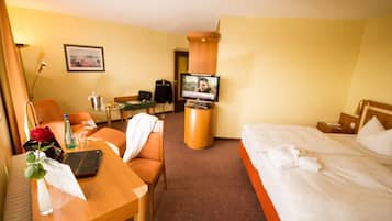 A hotel room with a bed, a desk with a laptop, a chair, a television, and a small table with a vase of flowers.