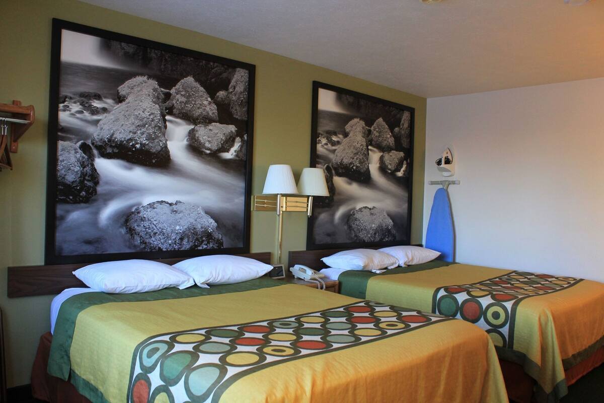 Een hotelkamer met twee bedden, een lamp en twee grote rotstekeningen aan de muur.