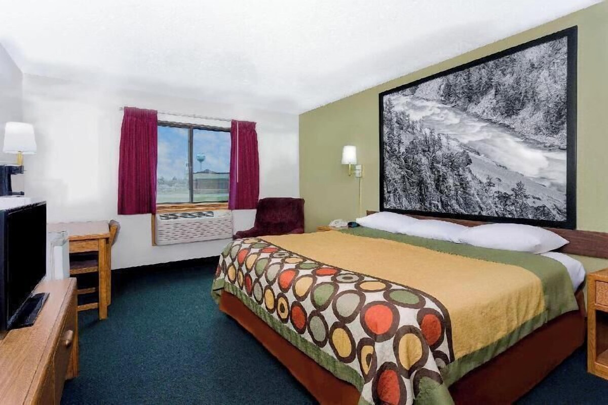 Une chambre d’hôtel avec un lit, un bureau, une chaise, une fenêtre avec des rideaux et un grand tableau encadré au mur.
