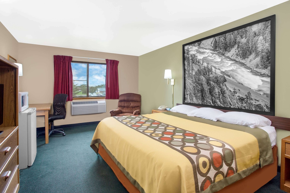 Ein Hotelzimmer mit Bett, Schreibtisch, Stuhl und einem großen Fenster mit Vorhängen.