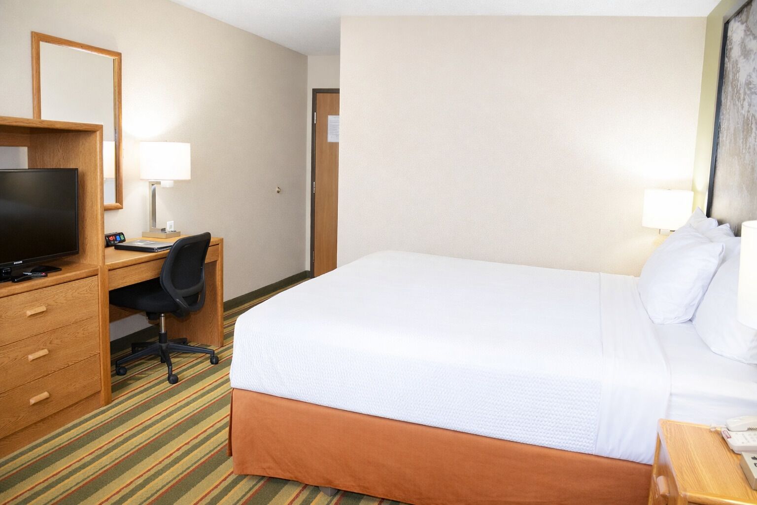 Una habitación de hotel con una cama, un escritorio con silla, televisor y teléfono.