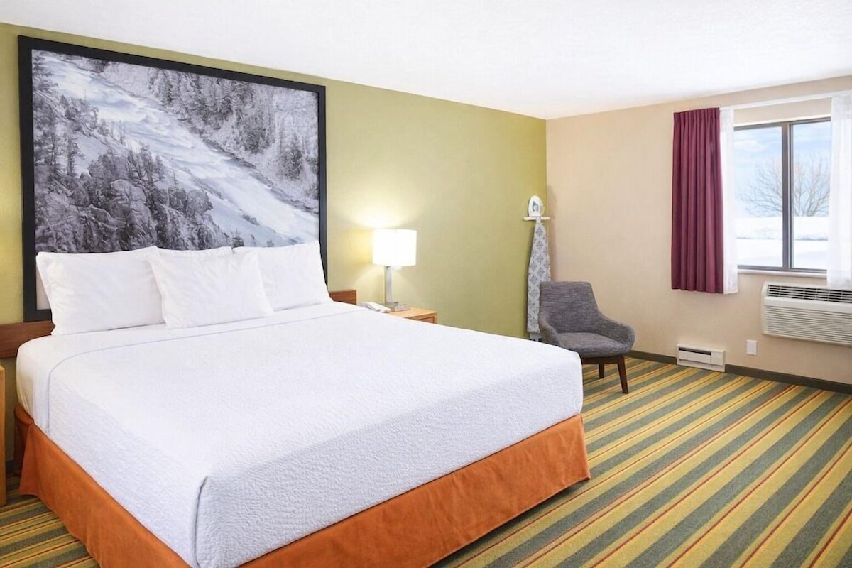 Ein Hotelzimmer mit einem großen Bett, einem Sessel, einem Gemälde, einer Lampe und einem Fenster.