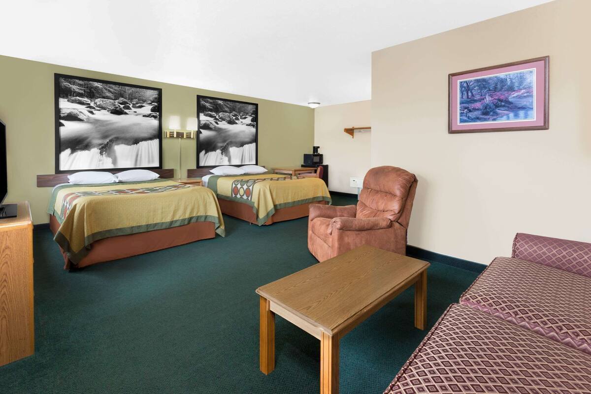 Een hotelkamer met twee bedden, een houten tafel, een bruine fauteuil en een bank.