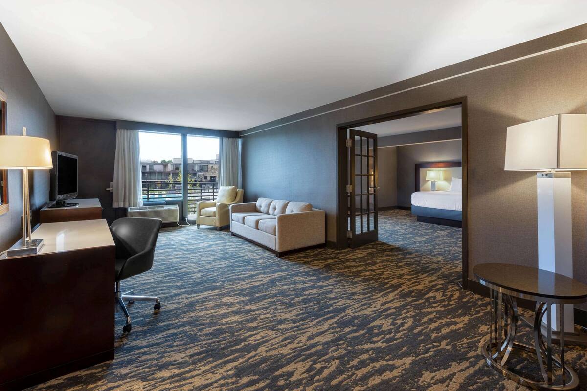 A hotel room with a desk, two chairs, a sofa, a bed, and a small table.