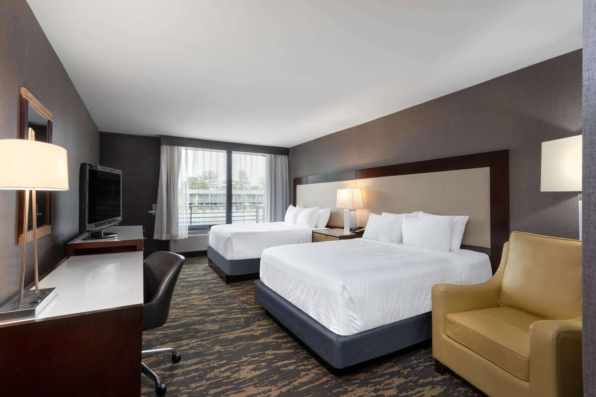 A hotel room with two beds, a desk, a chair, and a TV.