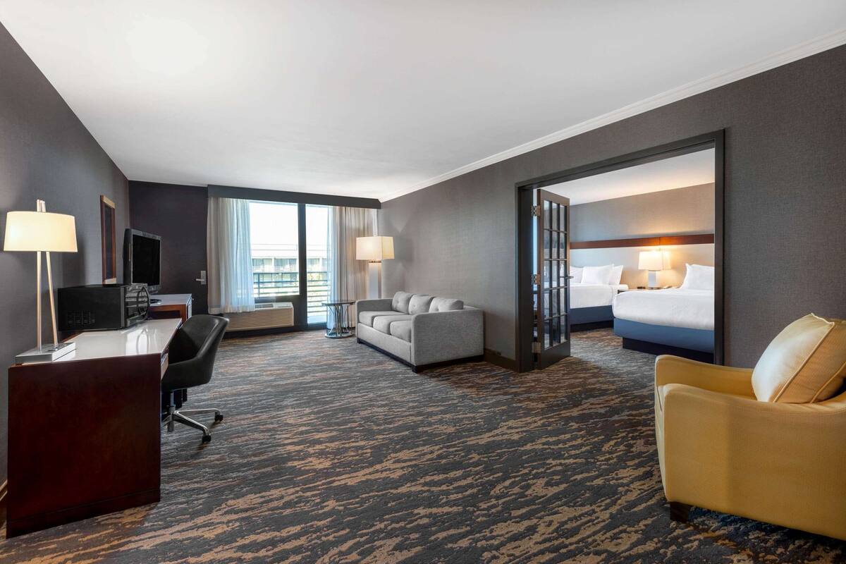 A hotel room with a desk, two couches, a bed, and a view of the city.