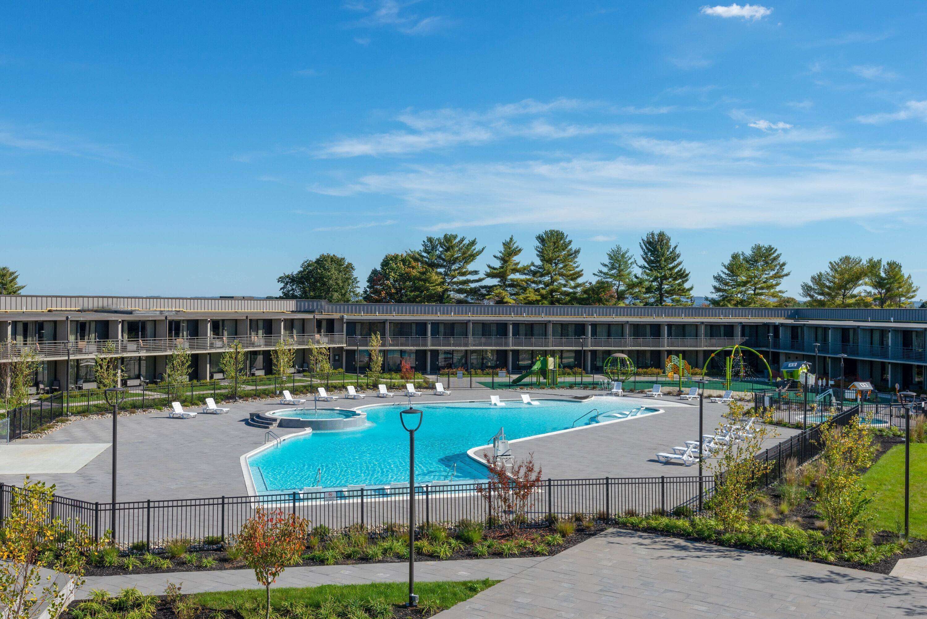 A modern building with a large swimming pool surrounded by lounge chairs and a landscaped area.