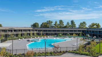 A modern building with a large swimming pool surrounded by lounge chairs and a landscaped area.