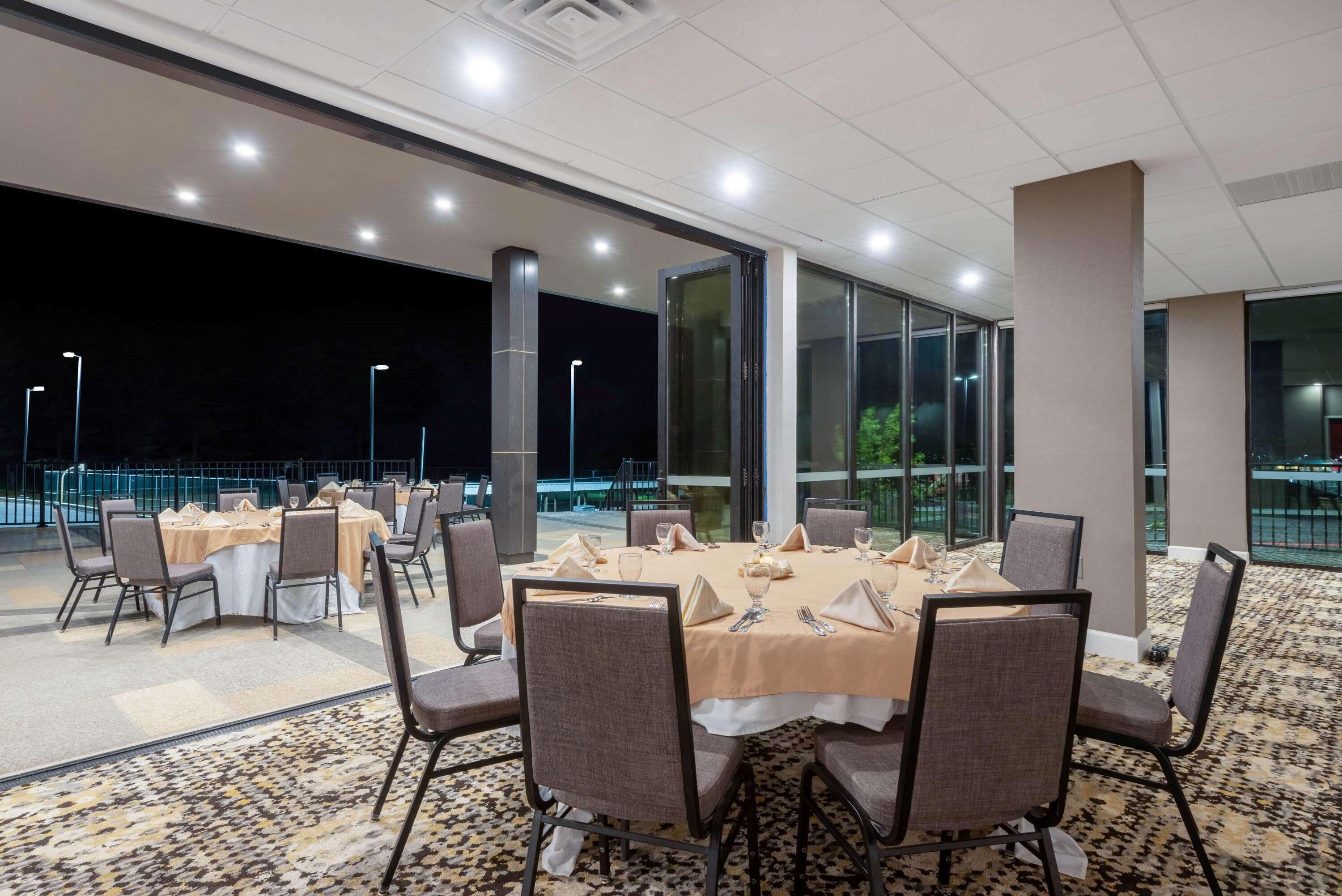 Una sala de banquets amb taules rodones preparades per dinar, envoltades de cadires i grans finestres que donen vistes a l'exterior.