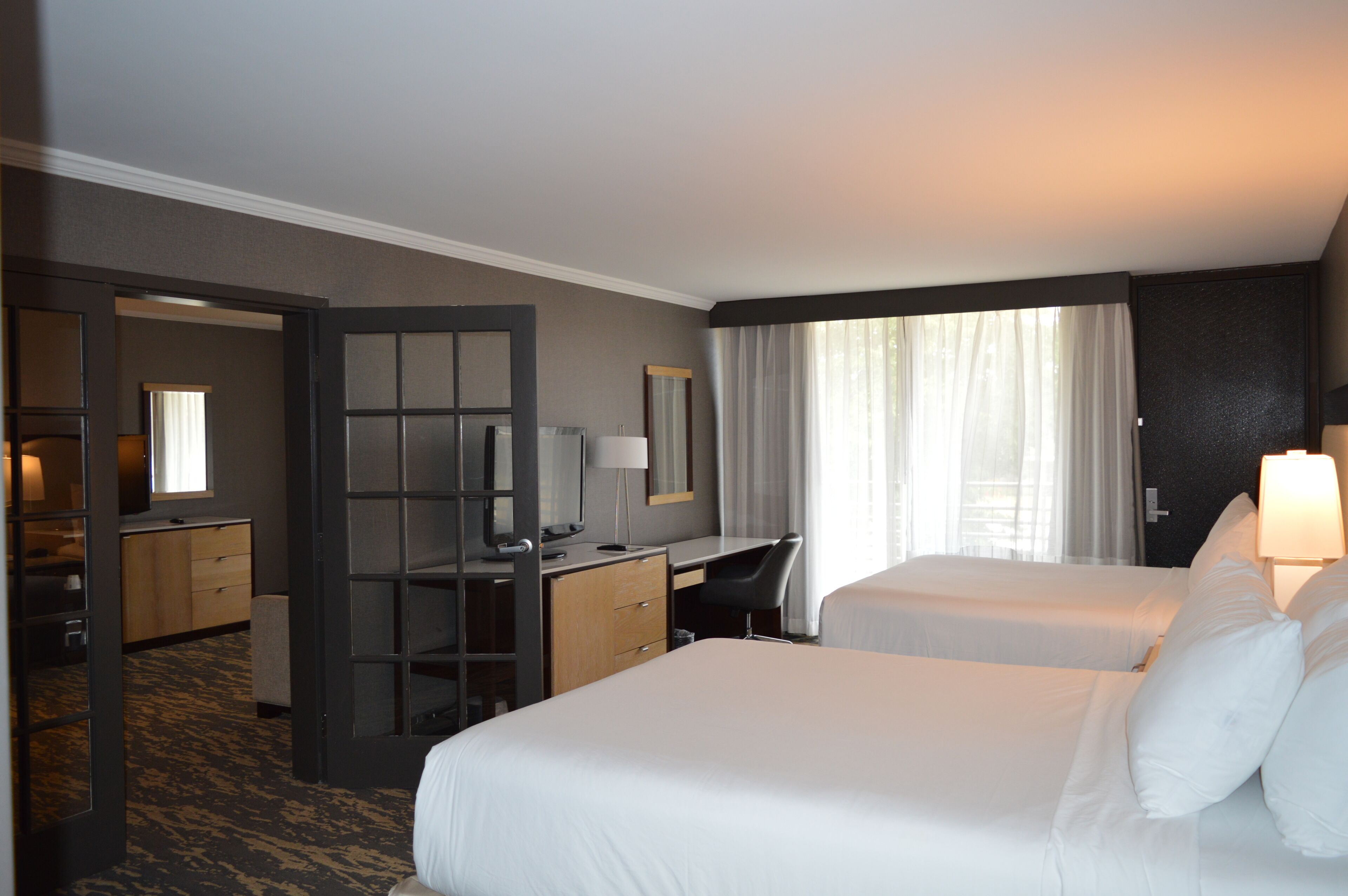 A hotel room with two beds, a desk, a chair, a dresser, and a mirror.