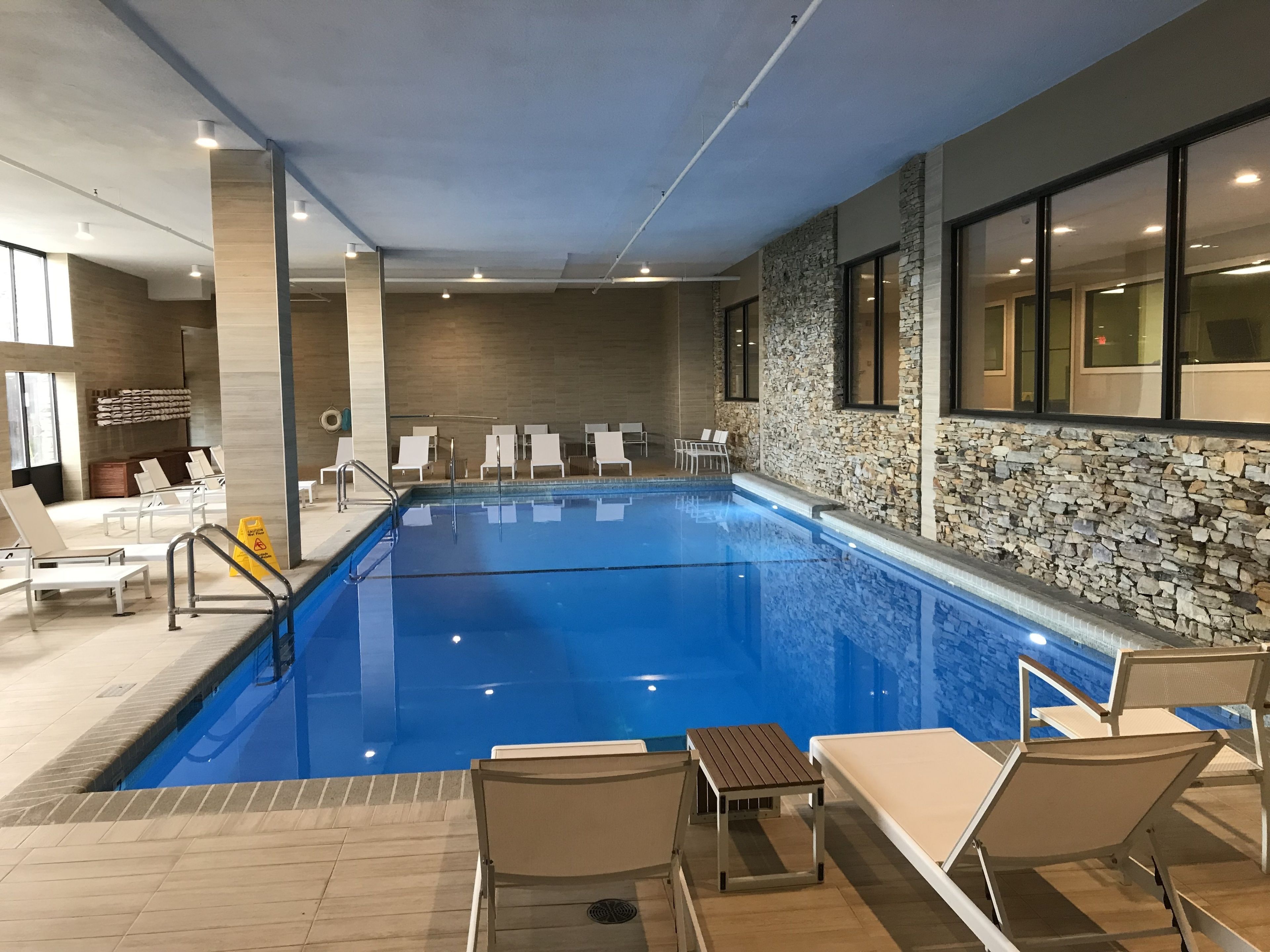 Une piscine intérieure dotée de chaises longues et d’un mur en pierre.