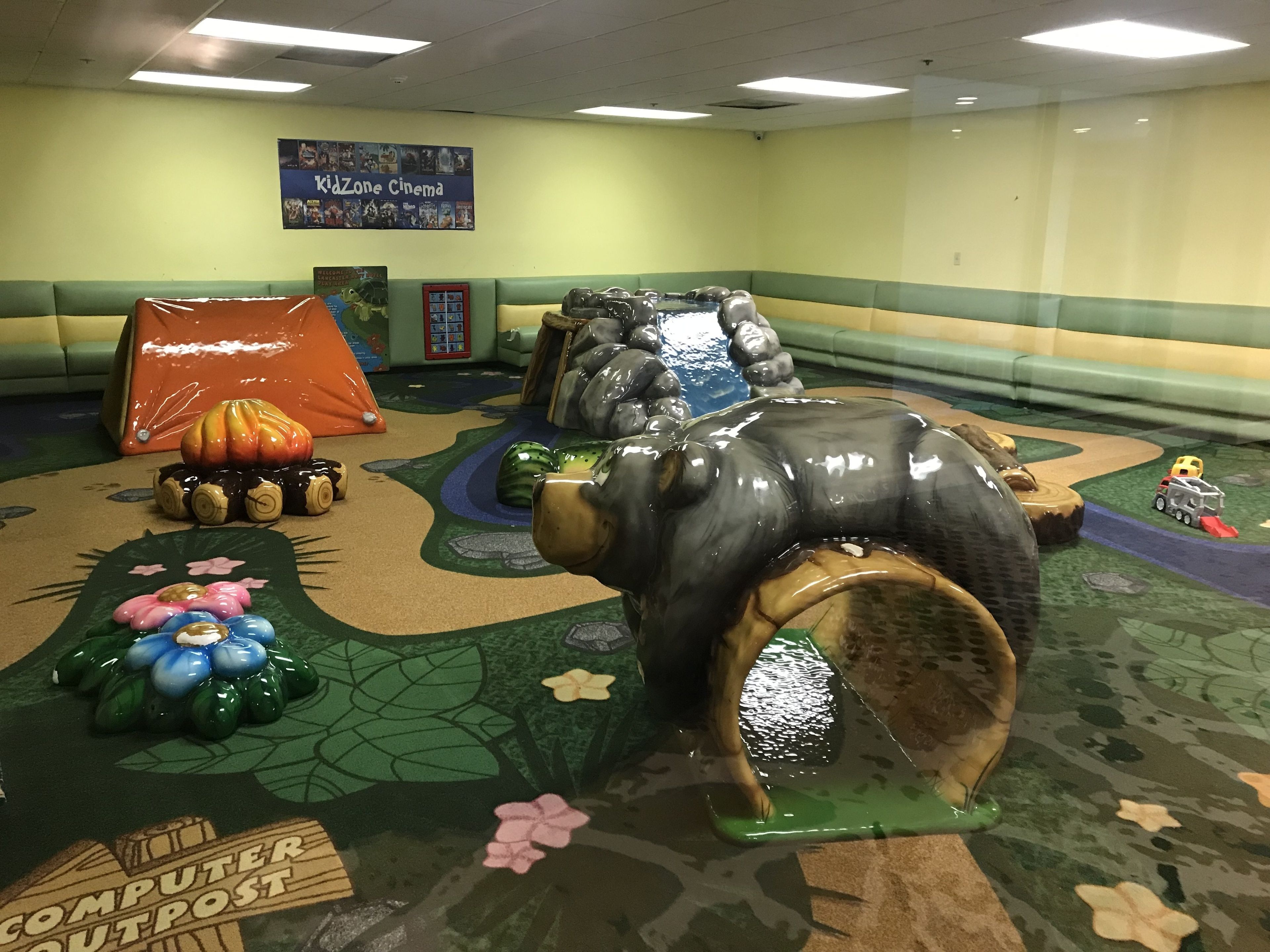 Un área de juegos interior con una gran escultura brillante de elefante, un coche pequeño y una tienda de campaña.