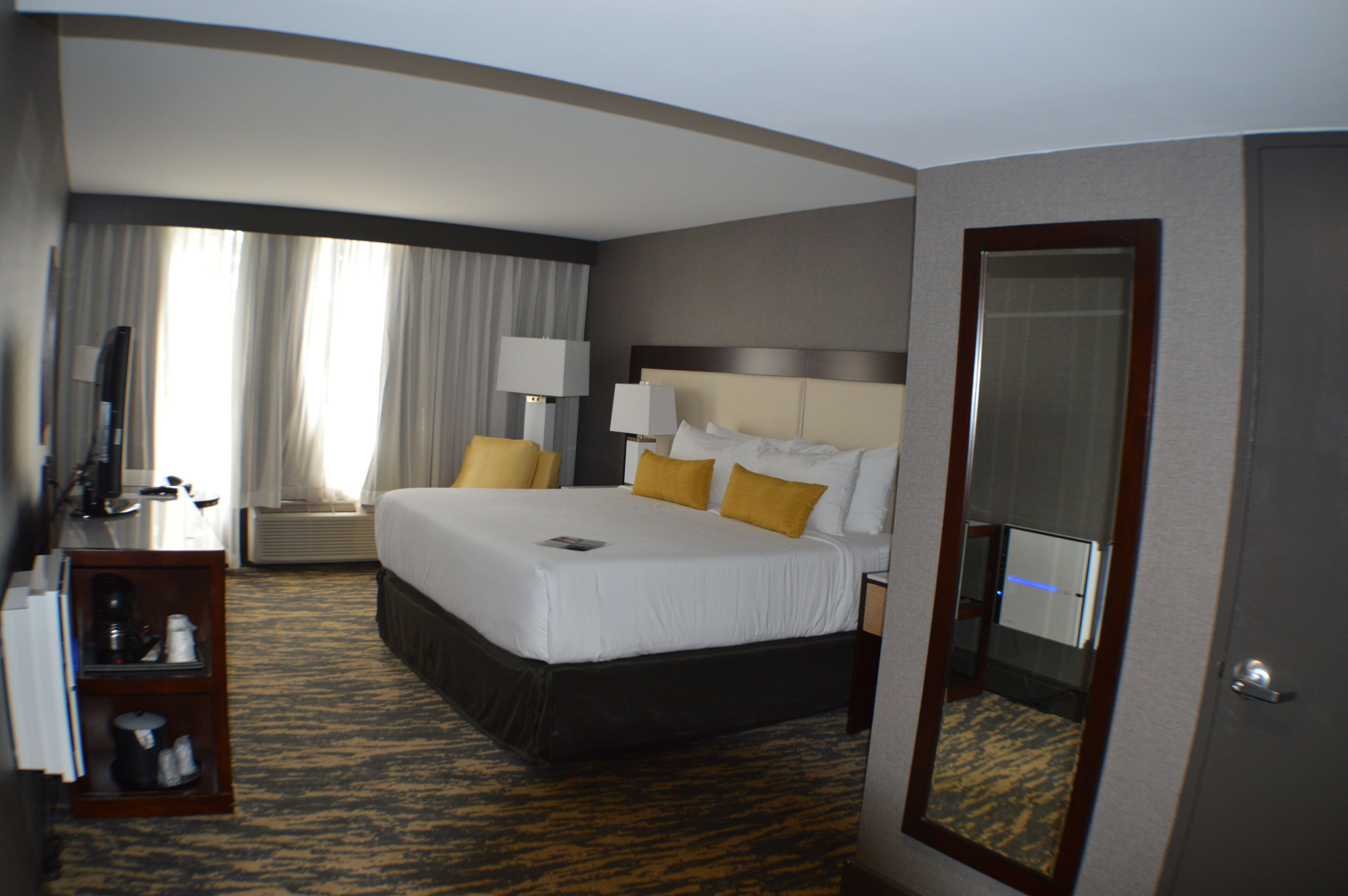 Une chambre d’hôtel avec un grand lit, deux lampes de chevet, une télévision, un bureau avec une lampe et un miroir.