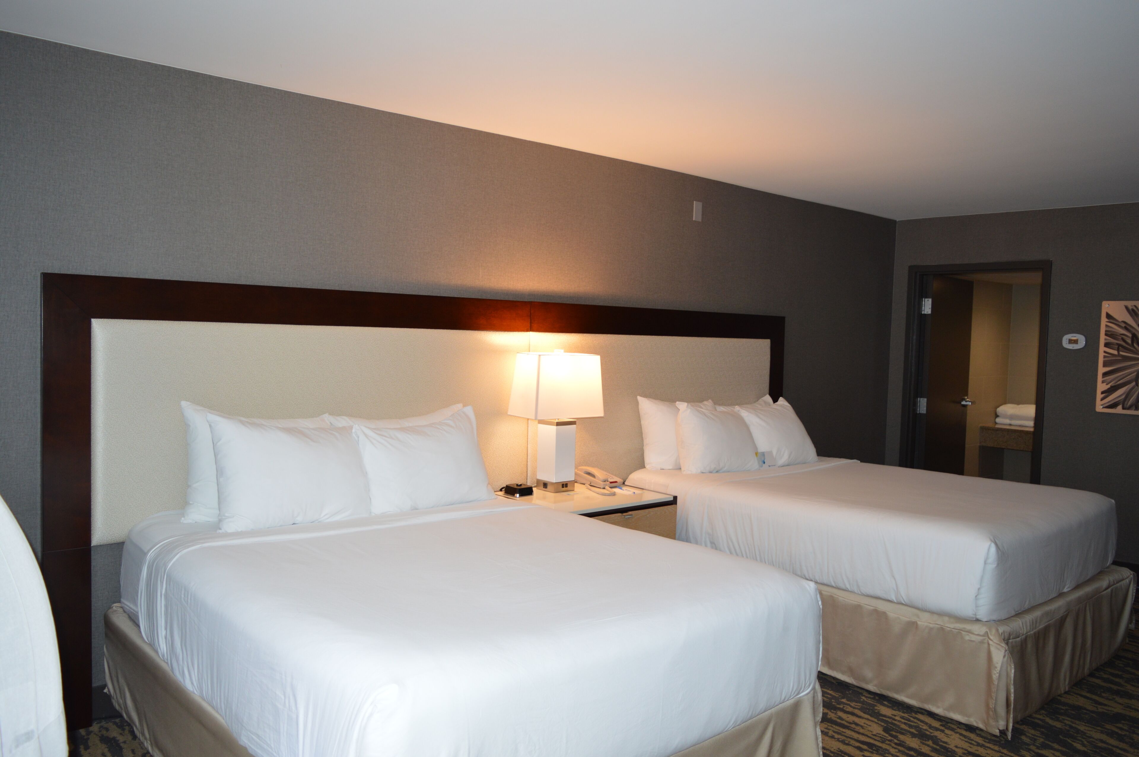 A hotel room with two beds, a nightstand with a lamp, and a mirror on the wall.