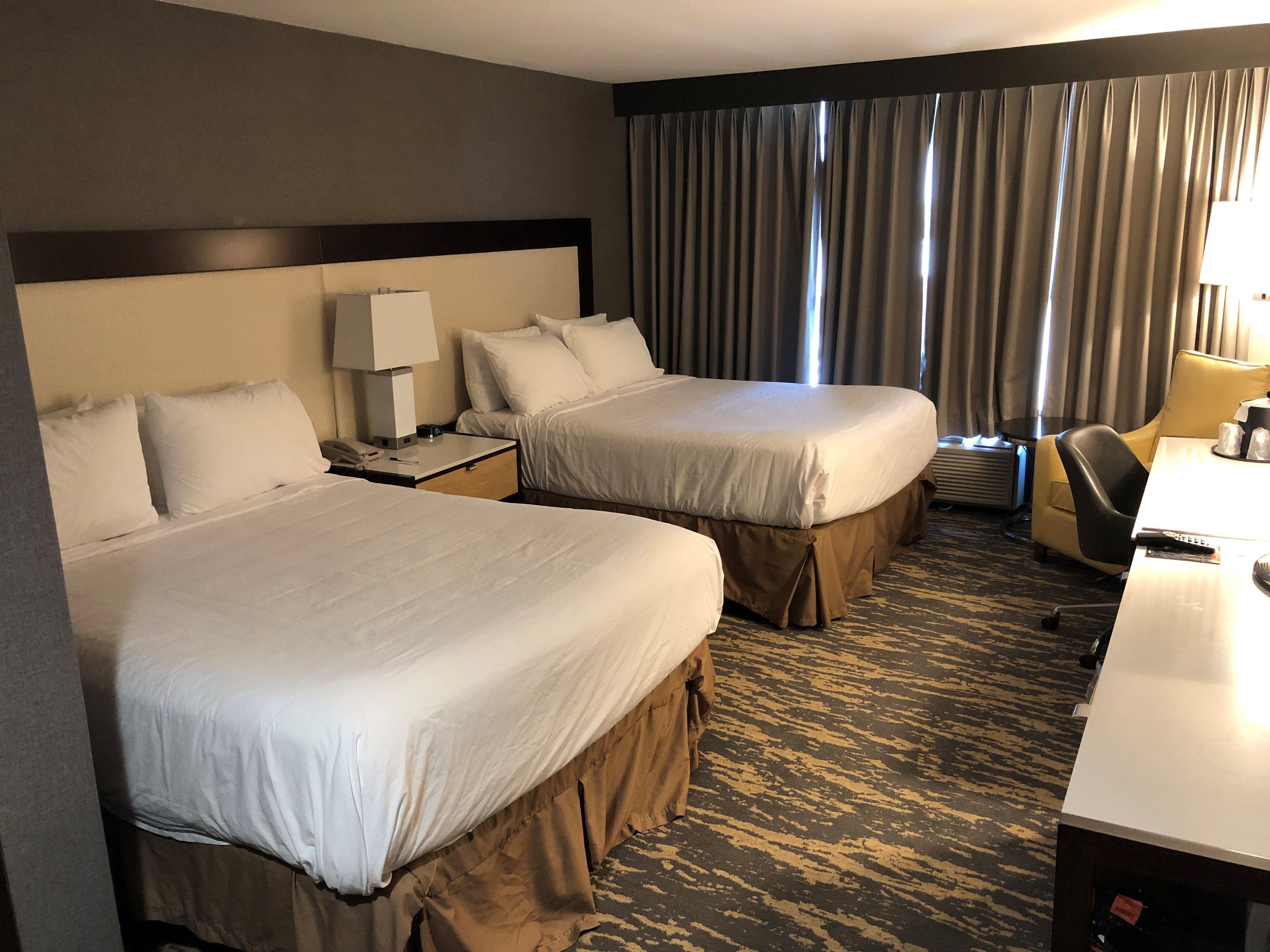 A hotel room with two beds, a desk, a chair, and a window with curtains.