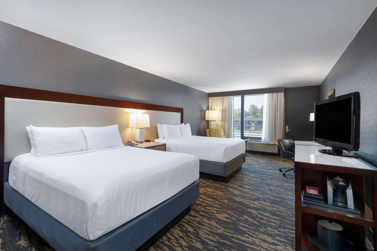 A hotel room with two beds, a desk, a television, and a window with curtains.