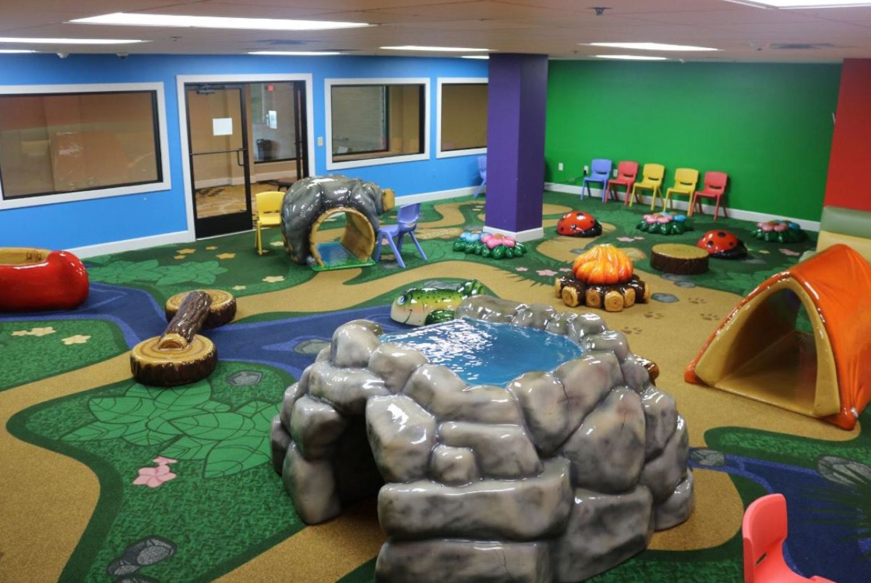 A playroom with a rock climbing area, a small pool, and colorful chairs.