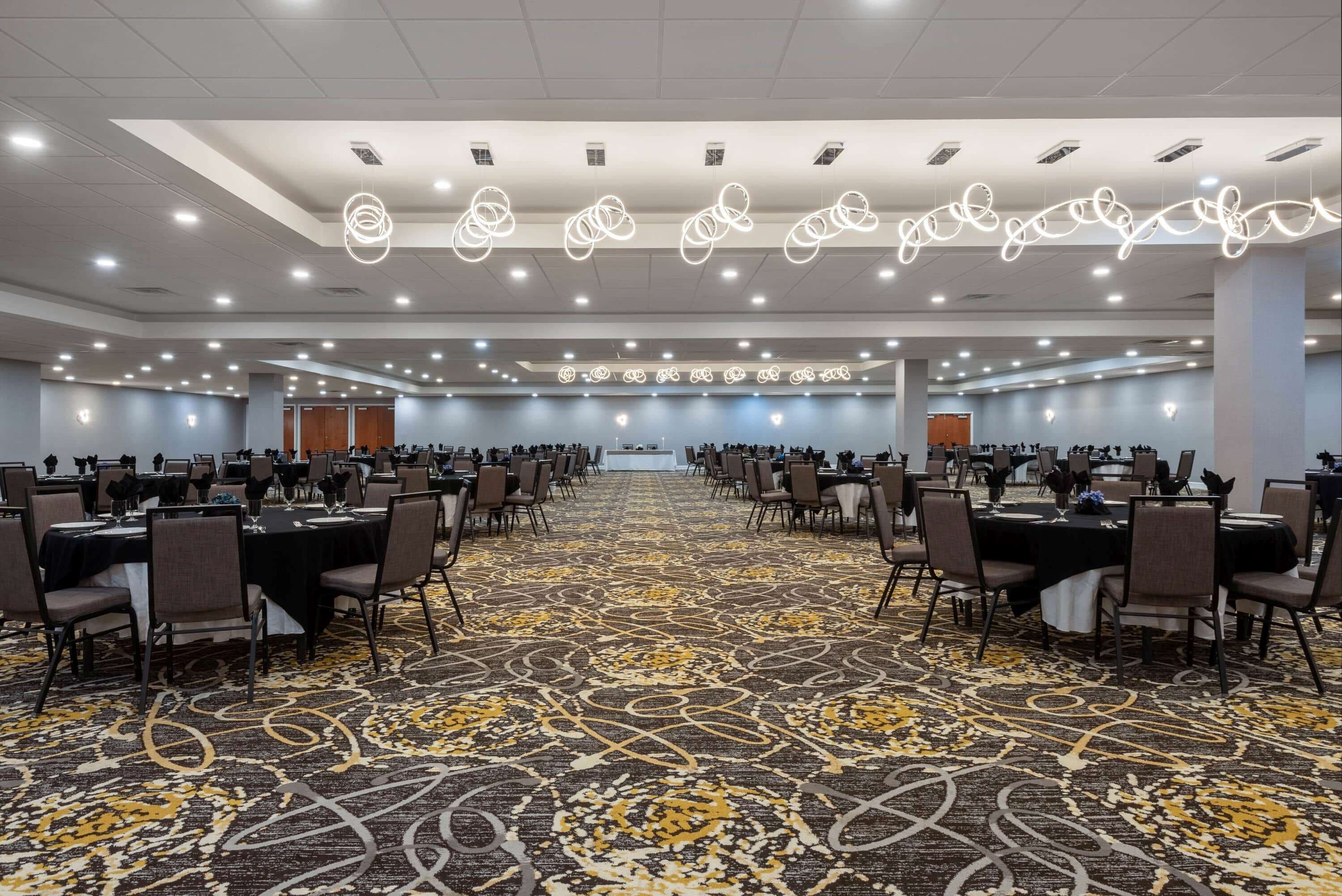 A large conference room with multiple tables and chairs, a patterned carpet, and ceiling lights.