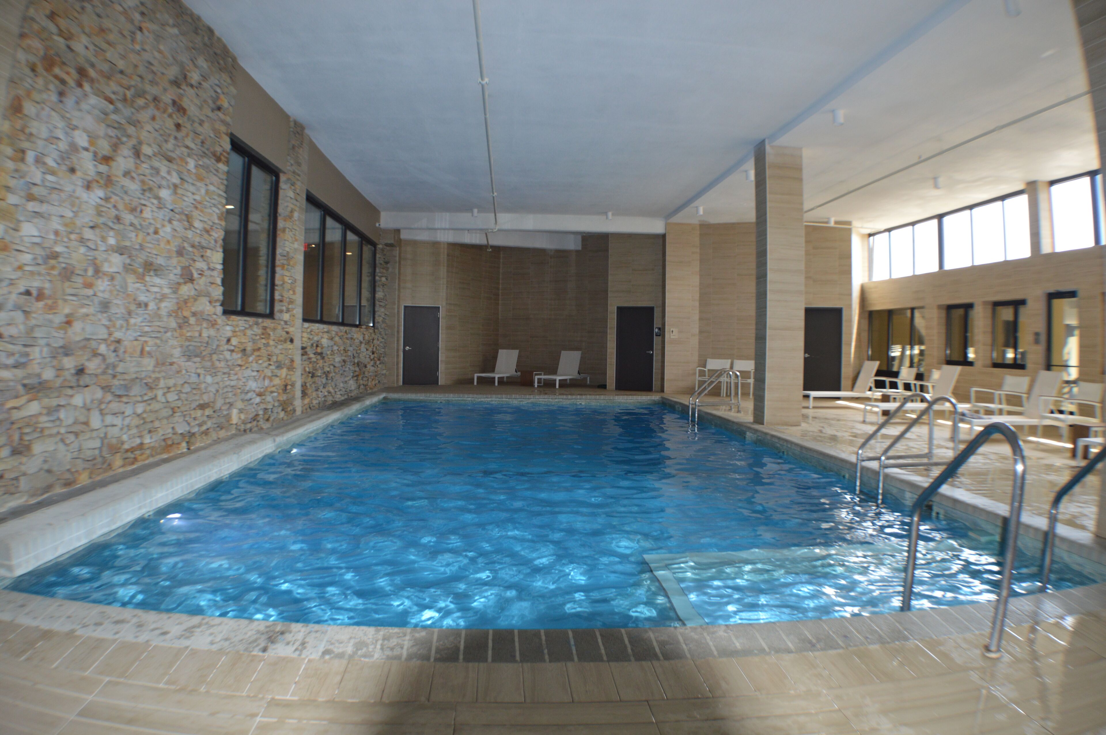 An indoor swimming pool with stone walls, clear blue water, and a tiled floor.