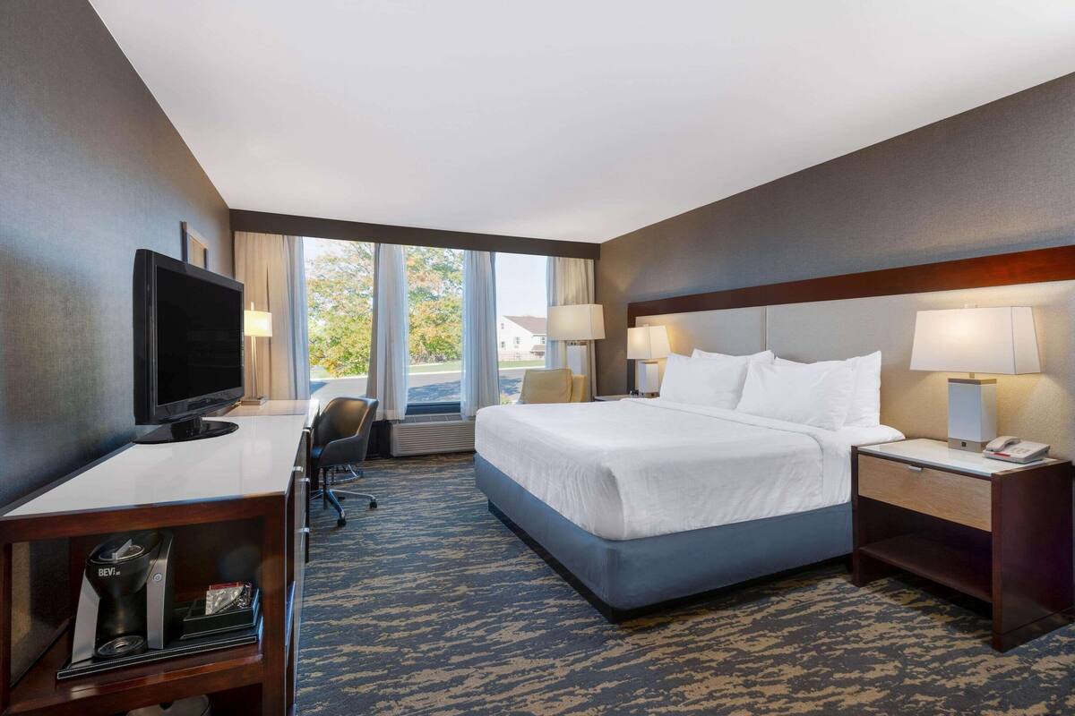 A hotel room with a large bed, a desk with a TV, a chair, and a desk lamp.