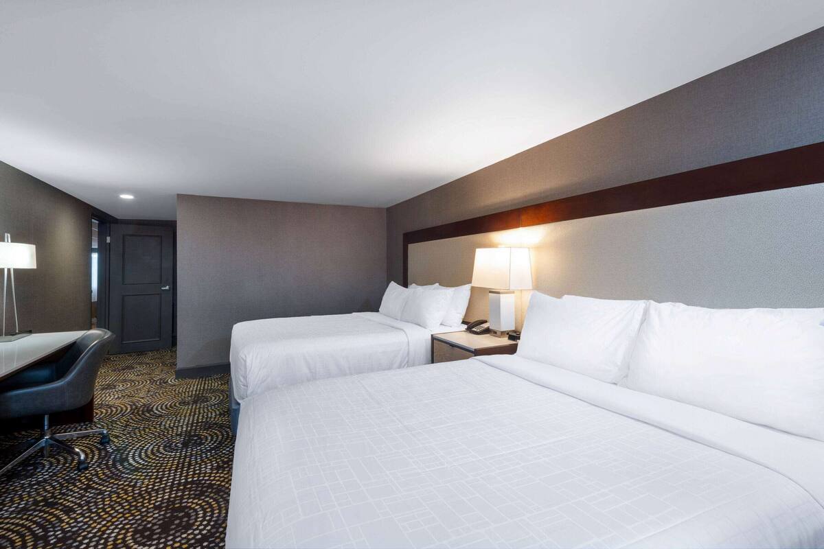 A hotel room with two beds, a desk, a chair, and a lamp.