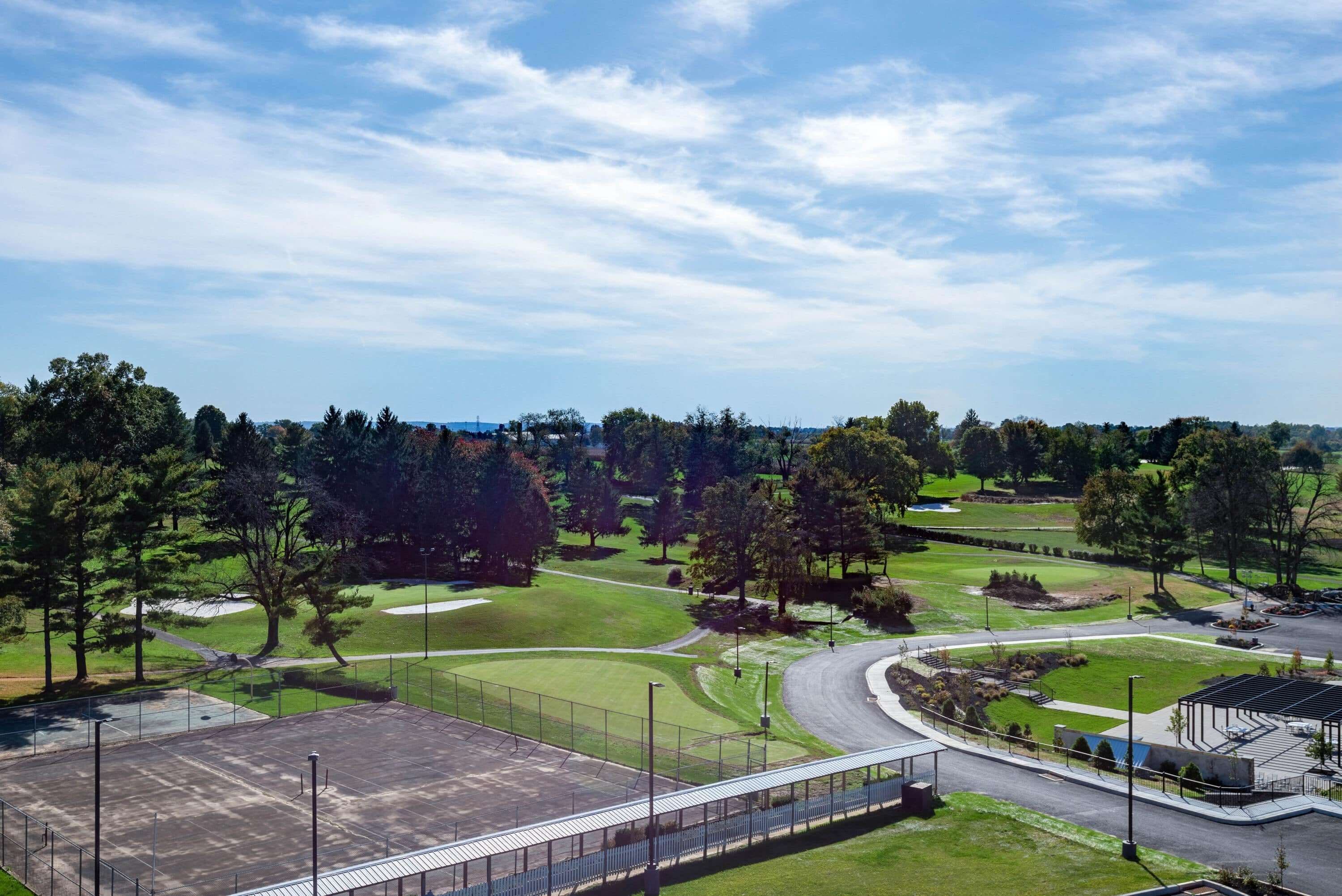 A golf course with a parking area, a covered seating area, and a pedestrian bridge.