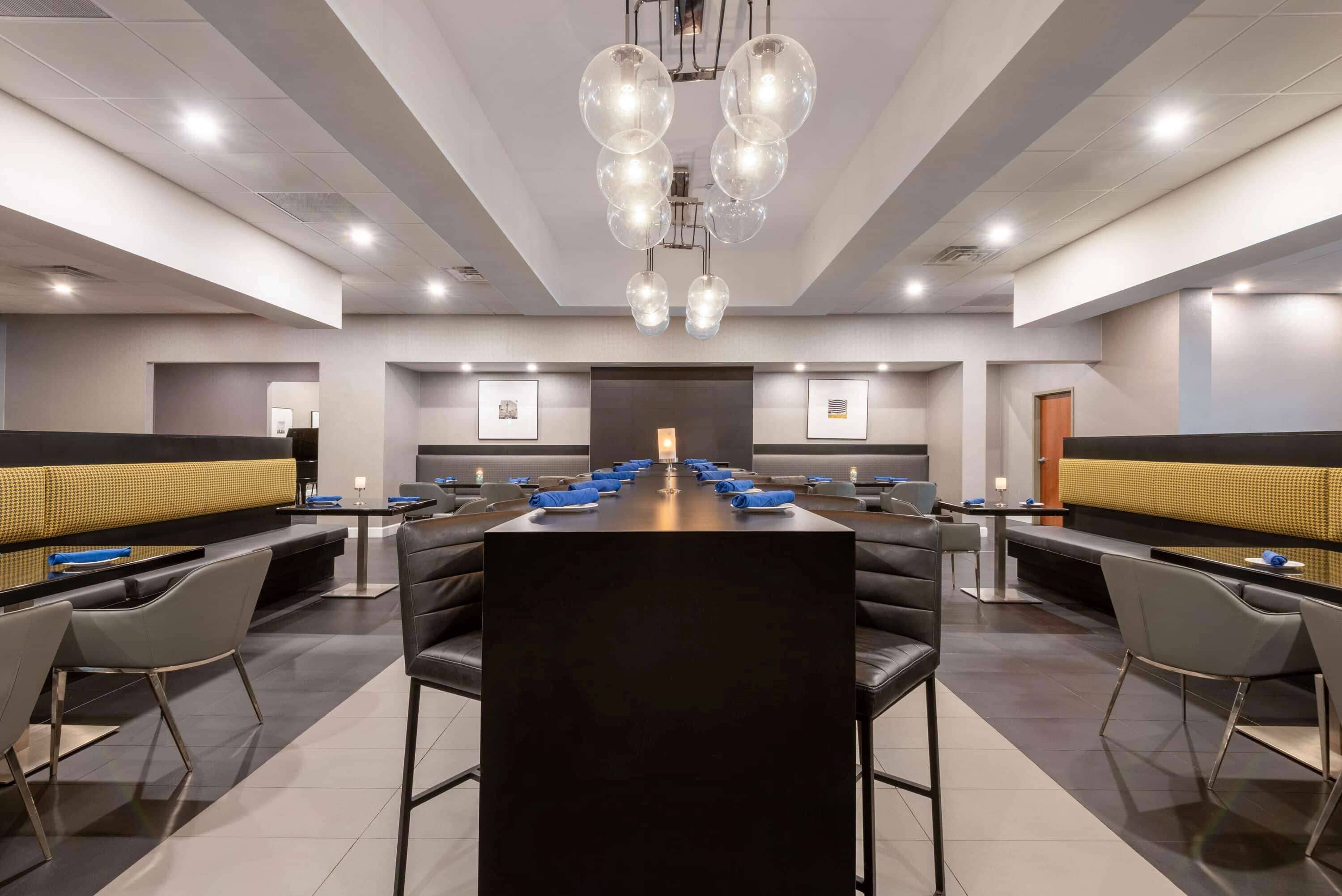 A modern dining area with a long table and chairs, a chandelier, and framed pictures on the walls.