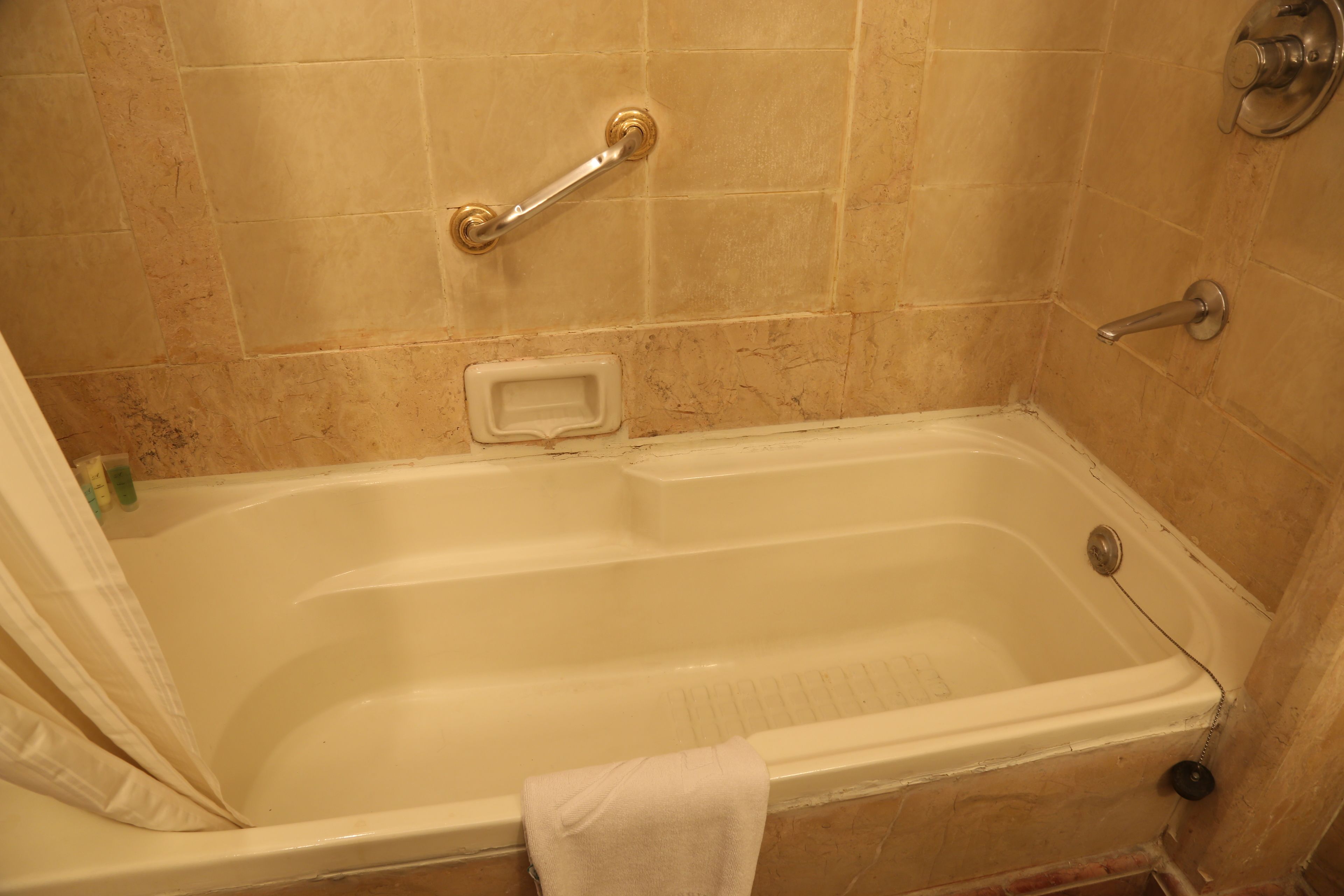 A bathtub with a grab bar, a towel, and a soap dish.