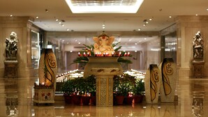 Un autel décoratif, orné d’une statue d’éléphant assis, est entouré de plantes en pot et de bougies allumées. Il est installé dans un hall spacieux et bien éclairé, agrémenté de colonnes et de statues en marbre.