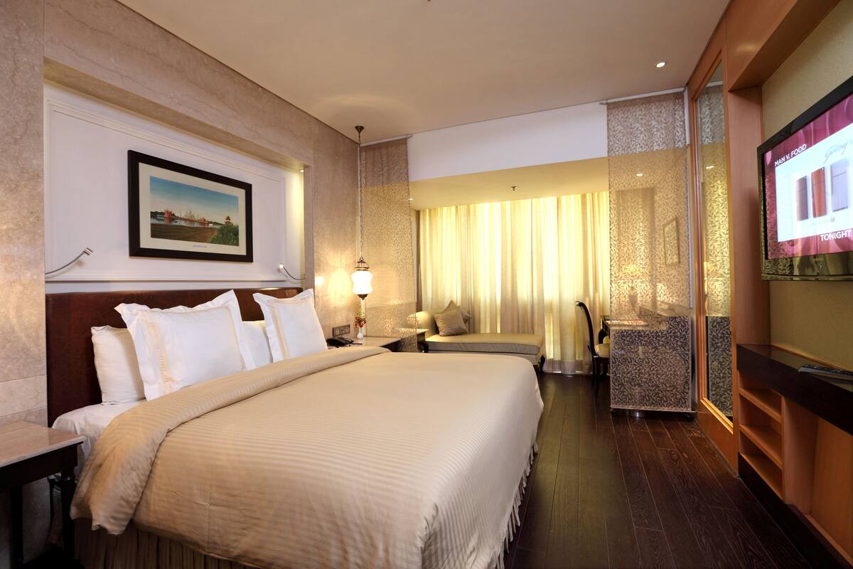 Une chambre d’hôtel avec un grand lit, un bureau, une chaise, une télévision et une fenêtre avec des rideaux.