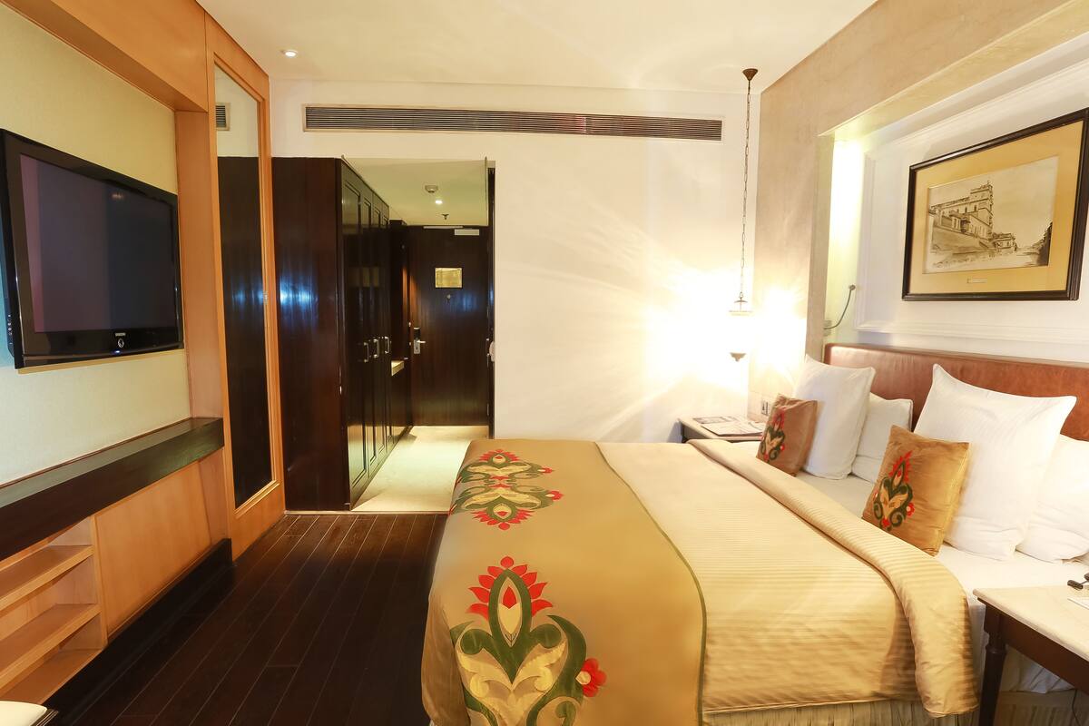 Une chambre d’hôtel comprenant un lit, une table de chevet, une lampe, une télévision, une armoire et un tableau encadré au mur.