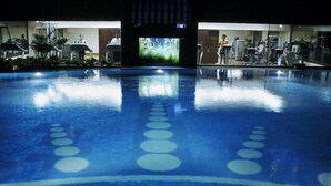 Une piscine dont l’eau reflète le matériel de gymnastique et un écran de télévision qui diffuse une image d’herbe.