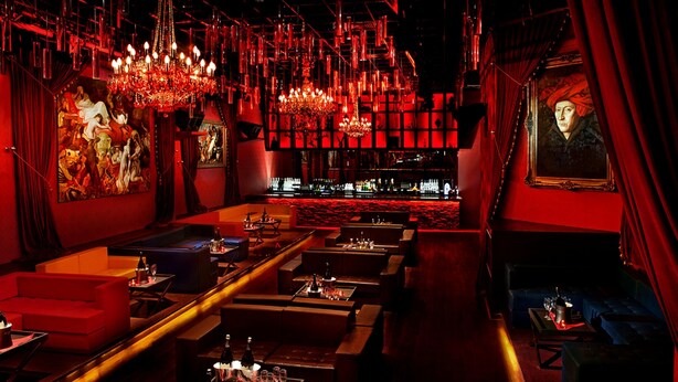 Un espace bar à la lumière tamisée, avec un éclairage d’ambiance rouge, différents types de sièges et un comptoir.