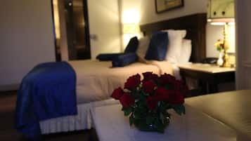 Una camera d'hotel con un letto, un comodino con una lampada e un vaso con rose rosse su un tavolo.