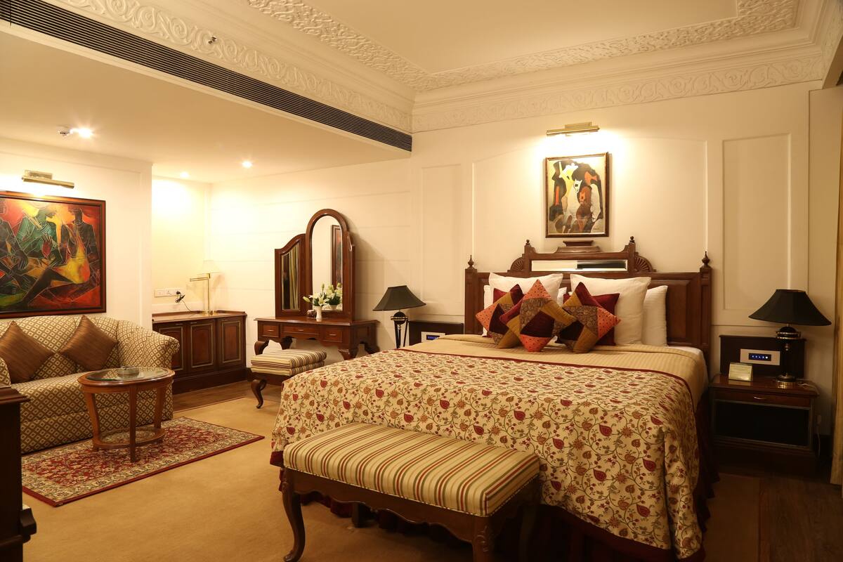 Une chambre d’hôtel dotée d’un grand lit, d’un coin salon avec un canapé et un fauteuil, d’une petite table d’appoint et d’une table de chevet avec une lampe.