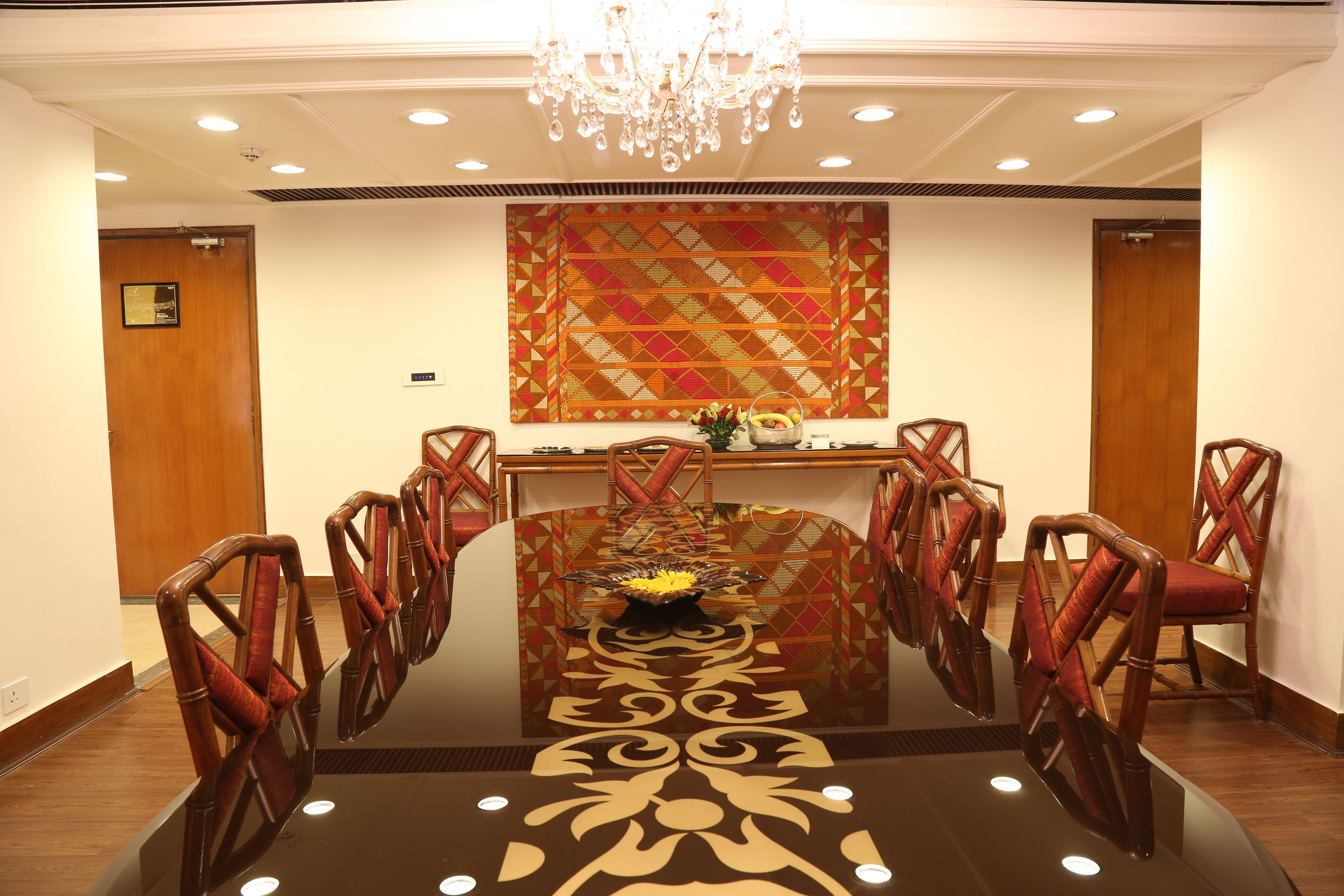 A conference room with a round table, wooden chairs, a chandelier, and a decorative wall panel.