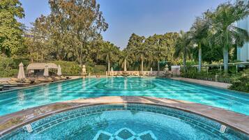 Relax by the serene pool surrounded by lush greenery and palm trees, with lounge chairs and umbrellas for a tranquil retreat.