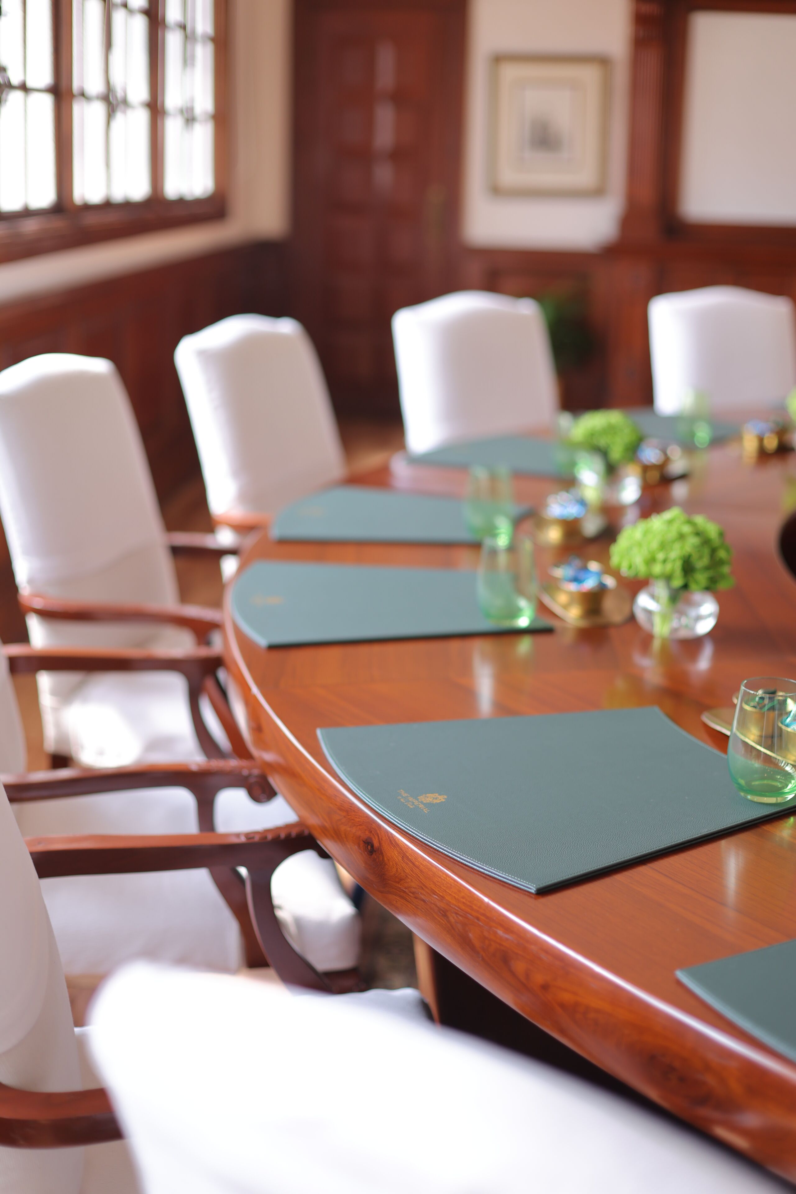 A conference room with a wooden table, white chairs, and green placemats.