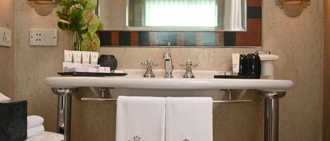 A bathroom with a white sink, two faucets, a mirror, and a towel rack with two towels.