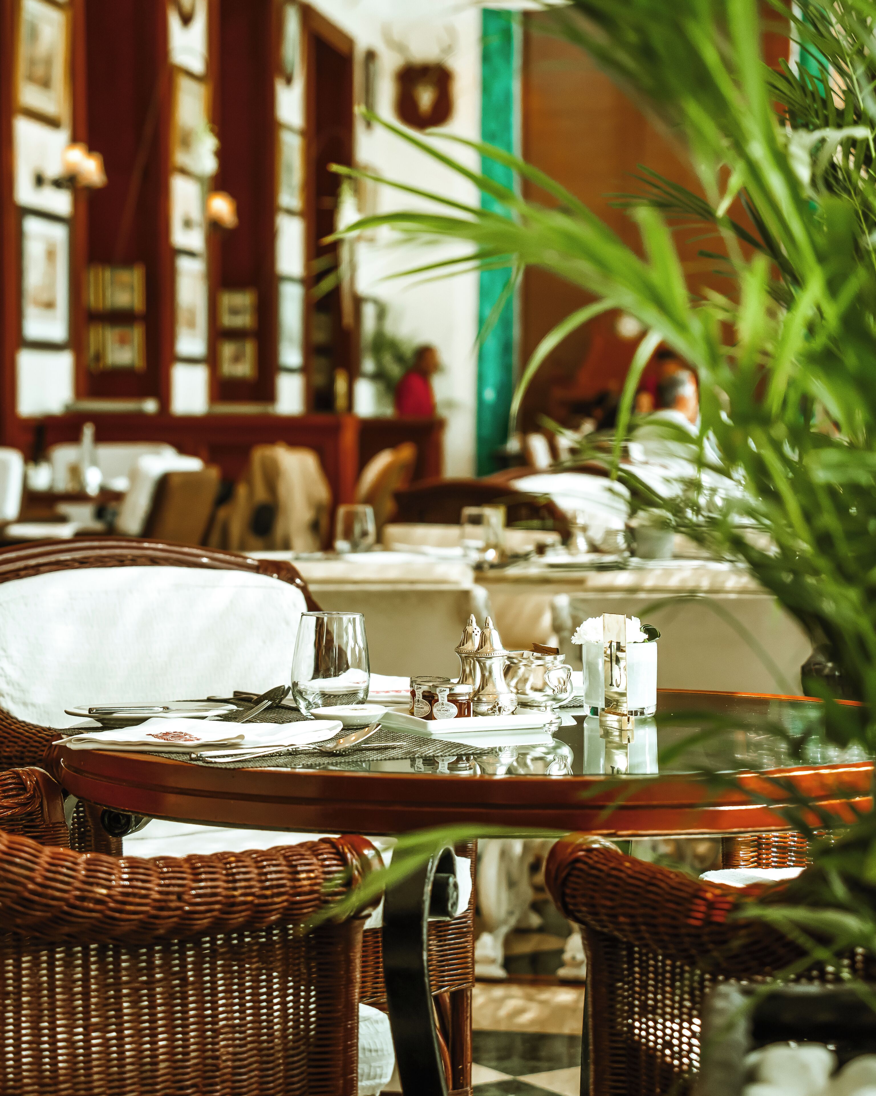 Zona pranzo con sedie in vimini, tavolo apparecchiato per due e vista dell'interno di un edificio con quadri appesi alle pareti.